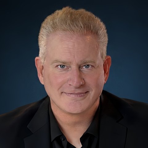 Studio headshot of Wylde Scott, author of Raising Dreamers and founder of The Imagination Project, in a black jacket against a deep navy background